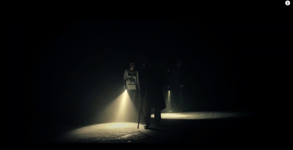 The cast makes their way through a dark warehouse with only a couple flashlights in Nightworld: Door of Hell